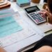 Pessoa faz contas com calculadora sobre documentos financeiros, ilustrando o crédito do Fies Empreendedor para quem quer empreender