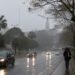 Avenida molhada sob chuva e neblina em cidade do Sul do país, com carros de farol aceso e pedestre de guarda-chuva, cenário previsto pelo INMET com a chegada da frente fria entre 18 e 20 de julho