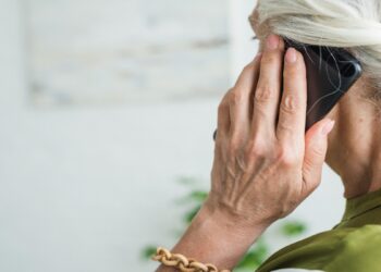 Mulher idosa de cabelos brancos fala ao telefone celular em casa, imagem que ilustra a matéria sobre o projeto que prevê devolução de valores a idosos vítimas de golpe digital
