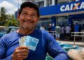 Pescador com notas de R$ 100 em frente a uma agência da Caixa, representando o pagamento do seguro-defeso previsto para esta terça