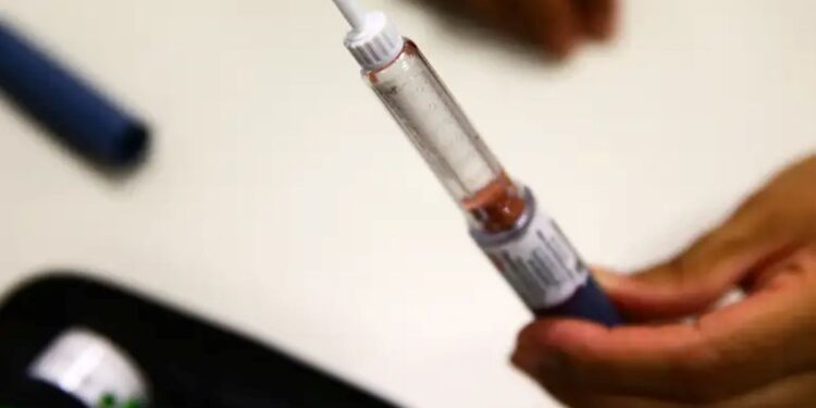 Mão segurando aplicador de semaglutida com líquido transparente e rótulo visível em superfície clara