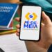 Celular com a marca do Pé-de-Meia nas mãos de um estudante, cuja conta depende da liberação feita pelo responsável legal na agência da Caixa