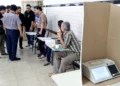 Imagem ilustrativa de mesários nas eleições com urna eletrônica em destaque.