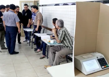 Imagem ilustrativa de mesários nas eleições com urna eletrônica em destaque.