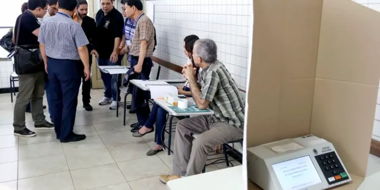 Imagem ilustrativa de mesários nas eleições com urna eletrônica em destaque.
