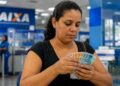 Beneficiária conta cédulas de real em agência da Caixa após o pagamento antecipado do Bolsa Família de julho de 2026 em cidades de seis estados