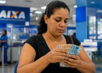 Beneficiária conta cédulas de real em agência da Caixa após o pagamento antecipado do Bolsa Família de julho de 2026 em cidades de seis estados