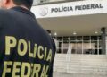 Agente de costas com o colete da Polícia Federal em frente a um prédio da corporação durante operação
