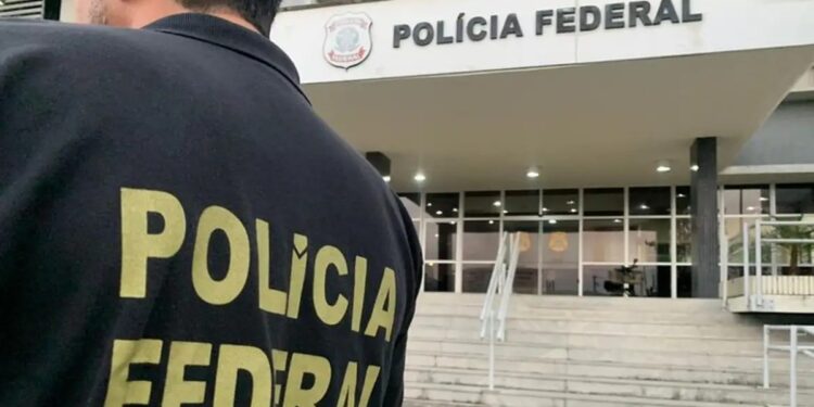 Agente de costas com o colete da Polícia Federal em frente a um prédio da corporação durante operação