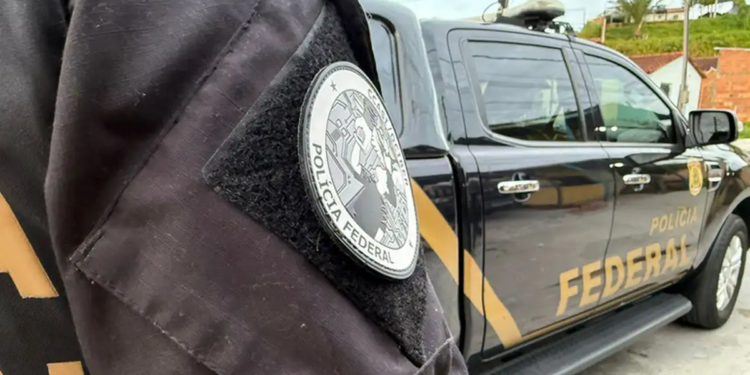 Brasão da Polícia Federal no uniforme de um agente, com viatura estacionada ao fundo