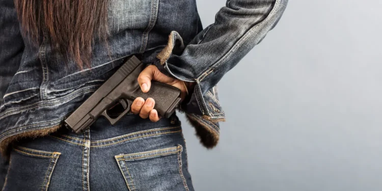 Mulher segurando uma arma de fogo na cintura, representando proposta que prevê porte temporário para mulheres com medida protetiva.