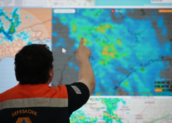 Imagem ilustrativa de agente da Defesa Civil apontando para um painel com imagens de radar meteorológico, em referência ao monitoramento durante o período de alerta