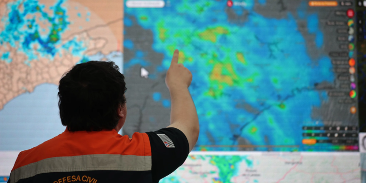 Imagem ilustrativa de agente da Defesa Civil apontando para um painel com imagens de radar meteorológico, em referência ao monitoramento durante o período de alerta