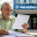 Homem idoso confere documentos em frente a uma agência da Previdência Social, representando a proposta de revisão do cálculo da aposentadoria do INSS