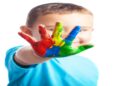 Criança sorridente mostra a mão pintada com várias cores, imagem associada à conscientização sobre o autismo e à defesa dos direitos das pessoas com TEA