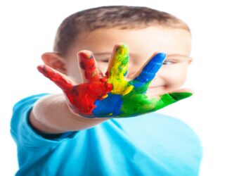 Criança sorridente mostra a mão pintada com várias cores, imagem associada à conscientização sobre o autismo e à defesa dos direitos das pessoas com TEA