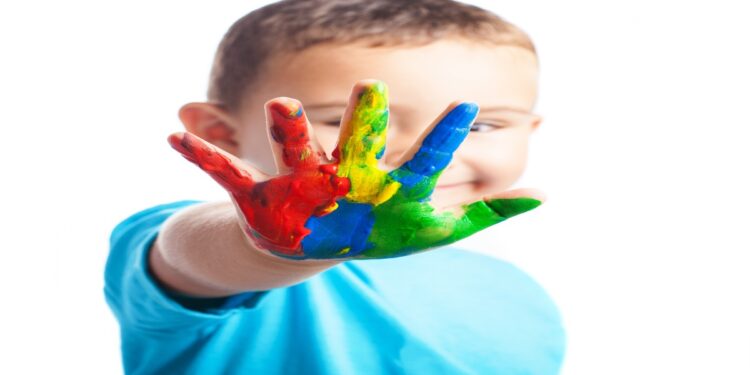 Criança sorridente mostra a mão pintada com várias cores, imagem associada à conscientização sobre o autismo e à defesa dos direitos das pessoas com TEA