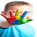 Criança sorridente mostra a mão pintada com várias cores, imagem associada à conscientização sobre o autismo e à defesa dos direitos das pessoas com TEA