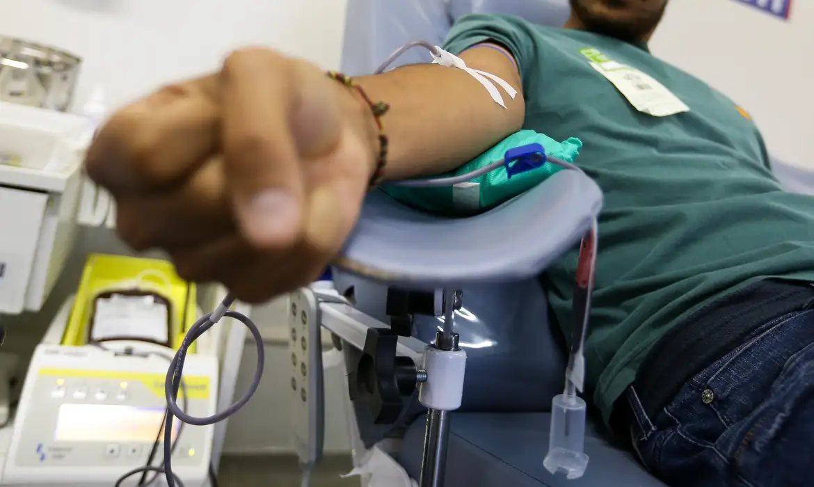 Homem doa sangue deitado na cadeira de coleta, cena que representa o direito à folga remunerada previsto na CLT