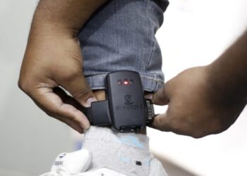 Detalhe de uma tornozeleira eletrônica de monitoramento sendo colocada no tornozelo de uma pessoa, imagem que ilustra a matéria sobre o projeto que obriga o agressor a pagar pelo dispositivo