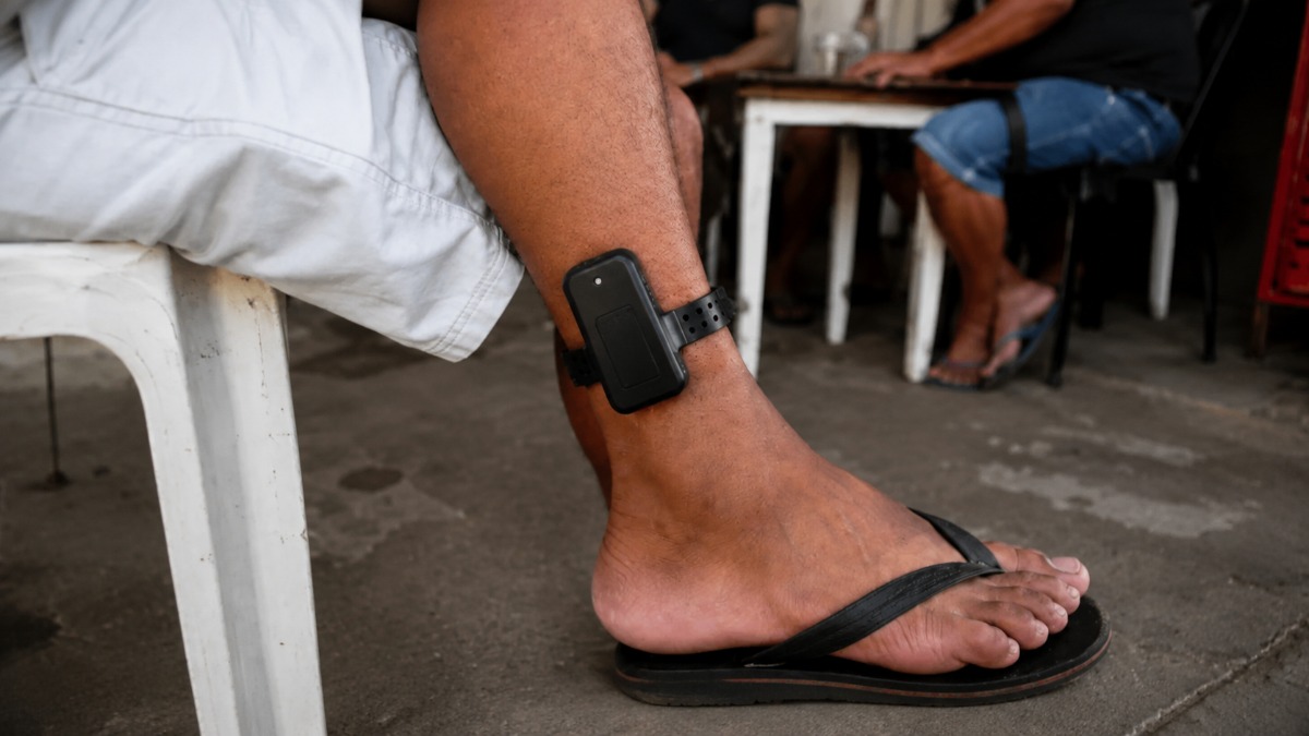 Homem sentado usa uma tornozeleira eletrônica de monitoramento na perna, imagem que ilustra a matéria sobre o projeto que obriga o agressor a pagar pelo dispositivo