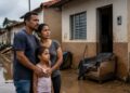 Família observa a rua alagada em frente à casa tomada pela lama após enchente, cena que ilustra a matéria sobre o projeto que suspende parcelas do Minha Casa, Minha Vida para vítimas de desastres