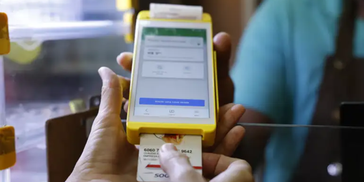 Cliente insere cartão de vale-alimentação em maquininha amarela durante pagamento em estabelecimento comercial