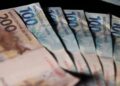 Notas de R$ 100 e R$ 200 espalhadas, representando o dinheiro do cashback do Imposto de Renda pago pela Receita Federal