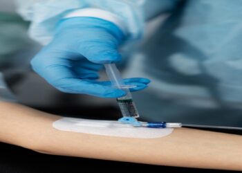 Profissional de luvas aplica uma seringa em um acesso na veia do braço de um paciente, cena que ilustra a matéria sobre o alerta da Anvisa contra a soroterapia em pessoas saudáveis