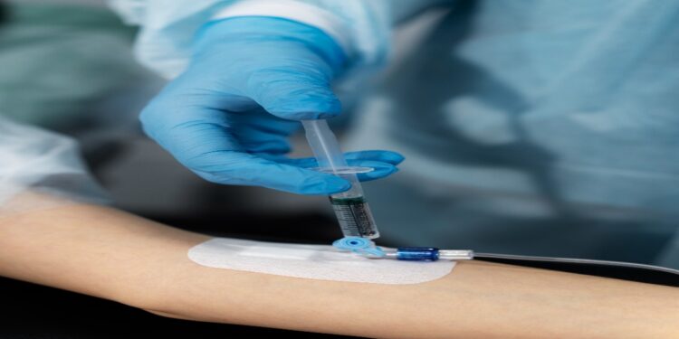 Profissional de luvas aplica uma seringa em um acesso na veia do braço de um paciente, cena que ilustra a matéria sobre o alerta da Anvisa contra a soroterapia em pessoas saudáveis