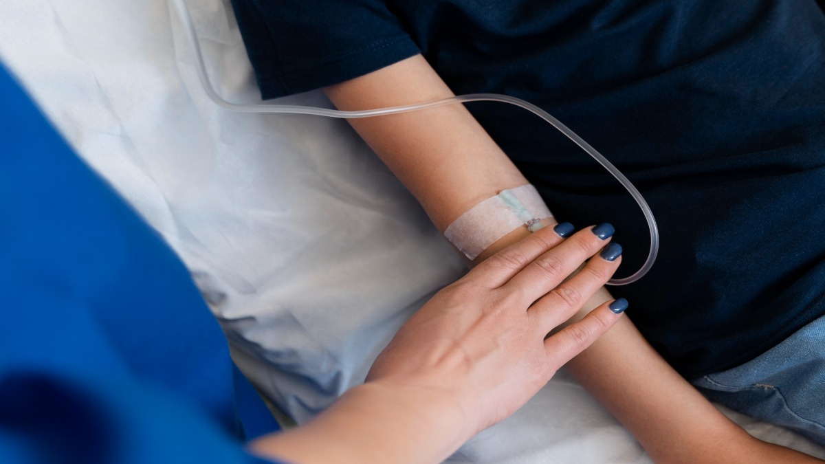 Braço de paciente com acesso intravenoso e curativo recebe soro por um tubo, imagem que representa a matéria sobre os riscos da soroterapia apontados pela Anvisa
