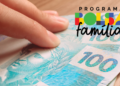Mão segurando notas de 100 reais ao lado do logo do Bolsa Família.