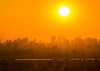 Pôr do sol intenso sobre metrópole com céu alaranjado.
