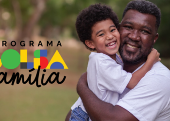 Homem adulto e criança sorridentes se abraçam ao ar livre ao lado do logo do Bolsa Família.
