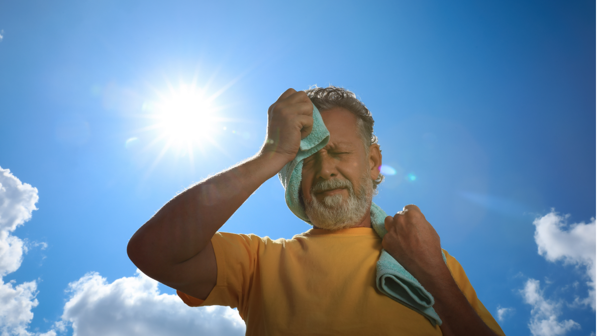 Homem enxuga o rosto sob sol forte em dia de calor intenso.