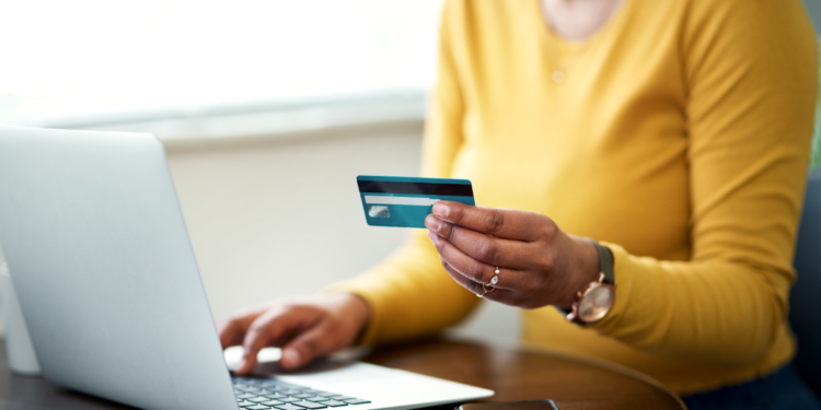 Mulher faz compra online utilizando cartão de crédito no notebook.