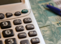 Planejamento financeiro com calculadora, notas de cem reais e caneta.