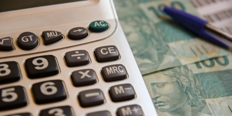 Planejamento financeiro com calculadora, notas de cem reais e caneta.
