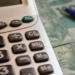 Planejamento financeiro com calculadora, notas de cem reais e caneta.