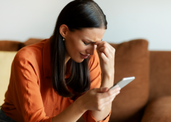 Jovem preocupada verifica mensagem no celular sentada no sofá.