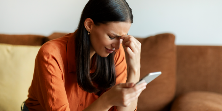 Jovem preocupada verifica mensagem no celular sentada no sofá.