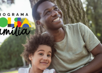 Homem e criança sorrindo com logo do Bolsa Família em parque arborizado.