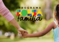 Mulher de blusa rosa e menina de trança de mãos dadas com logotipo do Bolsa Família ao fundo.