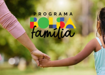 Mulher de blusa rosa e menina de trança de mãos dadas com logotipo do Bolsa Família ao fundo.