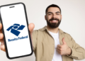Jovem exibe logo da Receita Federal no celular com gesto de aprovação.