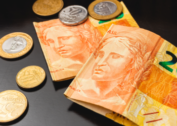 Cédulas de 20 reais e moedas brasileiras sobre mesa escura.