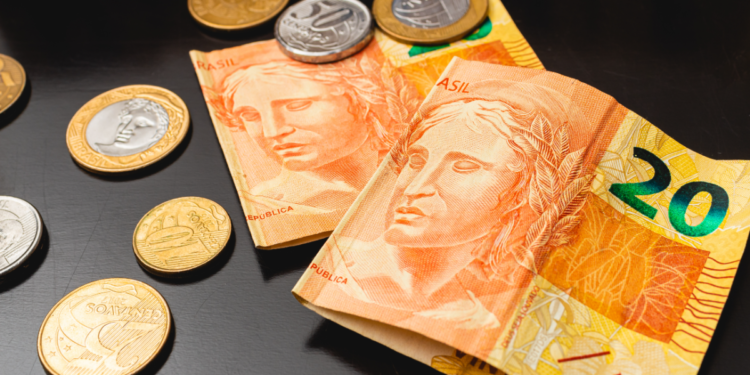 Cédulas de 20 reais e moedas brasileiras sobre mesa escura.