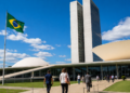 Pessoas caminhando pela rampa de acesso ao Congresso Nacional, com a bandeira do Brasil hasteada ao lado, em imagem ligada à votação do projeto sobre locação com desconto em folha.
