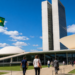 Pessoas caminhando pela rampa de acesso ao Congresso Nacional, com a bandeira do Brasil hasteada ao lado, em imagem ligada à votação do projeto sobre locação com desconto em folha.