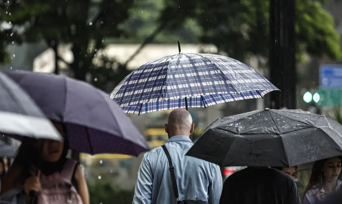 Imagem ilustrativa de pedestres protegidos por guarda-chuvas durante chuva em via urbana, tema da matéria sobre o alerta de ciclone extratropical emitido para a região Sul.